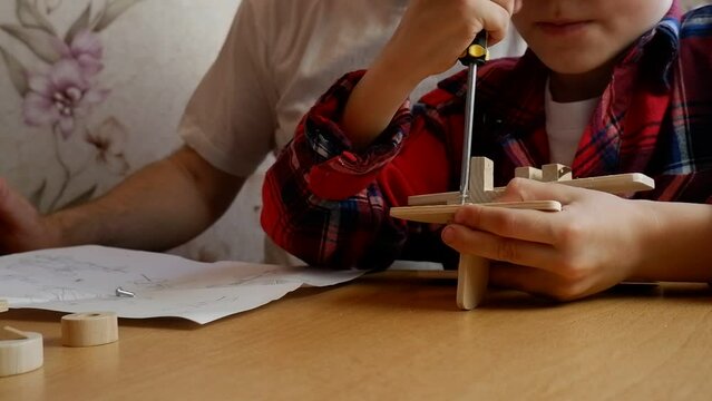 Happy father's day and childhood concept. Close-up of a father and a boy son in glasses work with hand tools, using a screwdriver, assembling a wooden house constructor at the table.