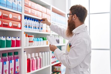 Young redhead man pharmacist reading prescription at pharmacy
