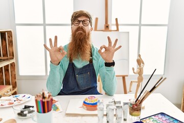 Redhead man with long beard painting clay bowl at art studio relax and smiling with eyes closed doing meditation gesture with fingers. yoga concept.