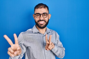 Middle east man with beard standing over blue background smiling looking to the camera showing...