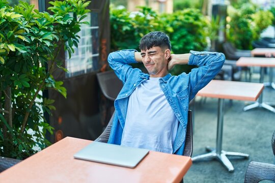 Young hispanic man stretching arms sitting on table at coffee shop terrace