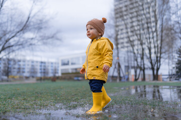 Happy little boy in yellow raincoat jumping in puddle after rain in autumn day.