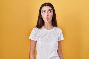 Fototapeta premium Young beautiful woman standing over yellow background making fish face with lips, crazy and comical gesture. funny expression.