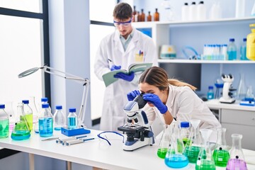 Fototapeta premium Young man and woman scientists workers using microscope at laboratory