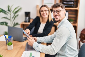 Young man and woman business workers using laptop and touchpad working at office