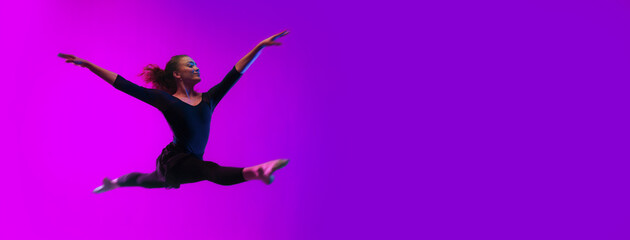 Modern dance girl dancer jumping up dancing in neon light doing gymnastic exercises in studio, wide...