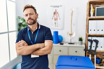 Middle age physiotherapist man working at pain recovery clinic skeptic and nervous, disapproving...
