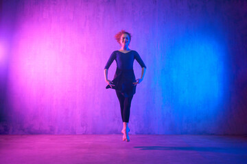 Modern dance girl dancer dancing in neon light doing gymnastic exercises in studio, copy space.