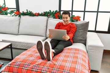 Young hispanic woman using laptop sitting by christmas decor at home