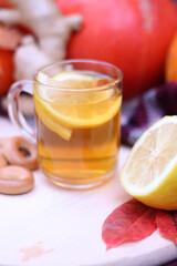 Glass cup with warm tea with lemon close-up on the background of pumpkins. Autumn composition with selective focus.