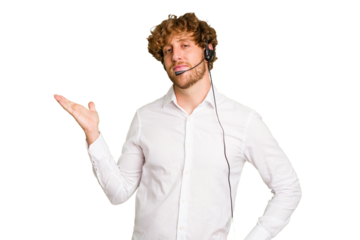 Telemarketer man working with a headset isolated on green chroma background showing a copy space on a palm and holding another hand on waist.