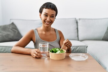 Young hispanic woman smiling confident eating salad at home