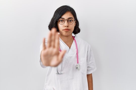 Young hispanic doctor woman wearing stethoscope over isolated background doing stop sing with palm of the hand. warning expression with negative and serious gesture on the face.