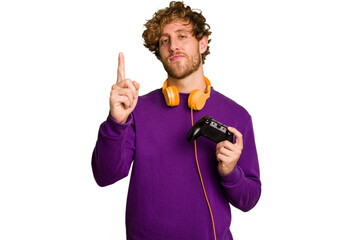 Young caucasian gamer man holding a game controller isolated on white background showing number one with finger. © Asier