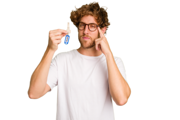 Young caucasian man holding home keys isolated on white background pointing temple with finger, thinking, focused on a task.
