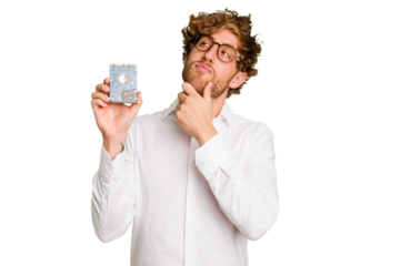 Young caucasian informatic man holding a hard drive isolated on white background looking sideways with doubtful and skeptical expression.