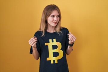 Blonde caucasian woman wearing bitcoin t shirt doing money gesture with hands, asking for salary...