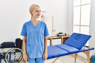 Obraz premium Beautiful caucasian physiotherapist woman working at pain recovery clinic smiling looking to the side and staring away thinking.