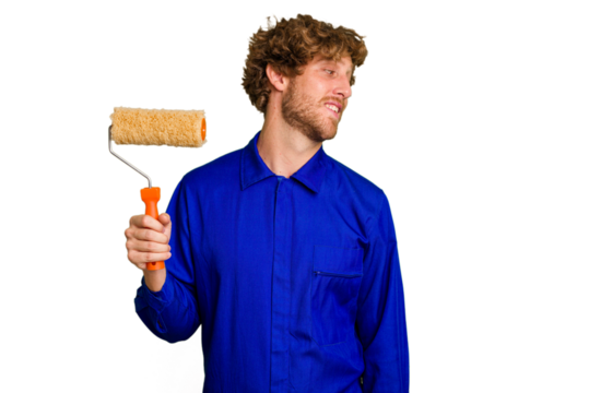 Young painter man holding a roll isolated on white background looks aside smiling, cheerful and pleasant.
