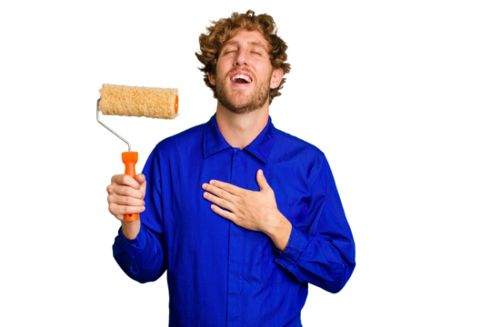 Young painter man holding a roll isolated on white background laughs out loudly keeping hand on chest.