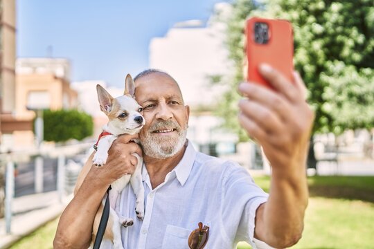 Senior man smihugging chihuahua making selfie by the smartphone at park