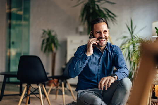 Smiling man making a phone call at the office, sitting indoors.