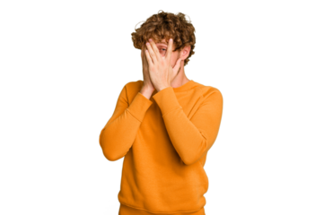 Young caucasian man isolated on green chroma background blink at the camera through fingers, embarrassed covering face.