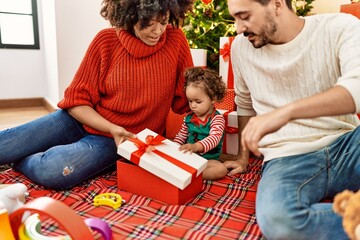 Couple and daughter unboxing gift sitting by christmas tree at home
