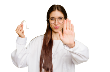 Young otorhinolaryngologist caucasian woman holding hearing aid isolated standing with outstretched hand showing stop sign, preventing you.