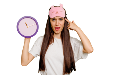 Young caucasian woman wearing pajama and holding a clock showing a disappointment gesture with forefinger.