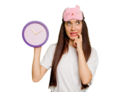 Young caucasian woman wearing pajama and holding a clock relaxed thinking about something looking at a copy space.