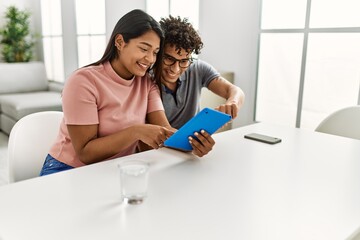 Young latin couple smiling happy using touchpad sitting on the sofa at home.