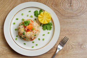 Fried rice with smoked salmon,green peas,carrots,onions,garlics,spring onions,soy sauce and peppers on plate with wooden background.Top view.Copy space