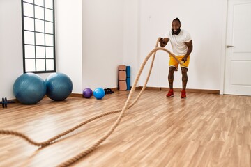 Young african american man smiling confident training with battle rope at sport center