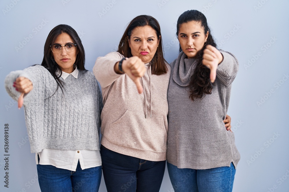 Sticker Mother and two daughters standing over blue background looking unhappy and angry showing rejection and negative with thumbs down gesture. bad expression.