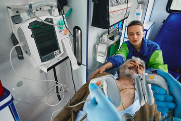 First aid in ambulance. Paramedic with defibrillator pads before CPR for casualty man inside ambulance © Peakstock