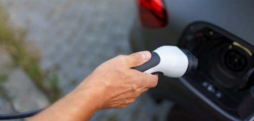 Man holding power supply cable at electric vehicle charging station, closeup