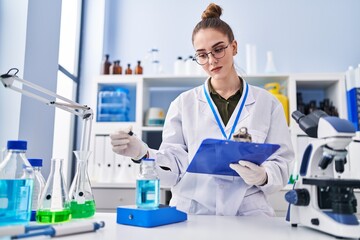 Young woman scientist reading document measuring liquid at laboratory