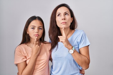 Young mother and daughter standing over white background thinking concentrated about doubt with...