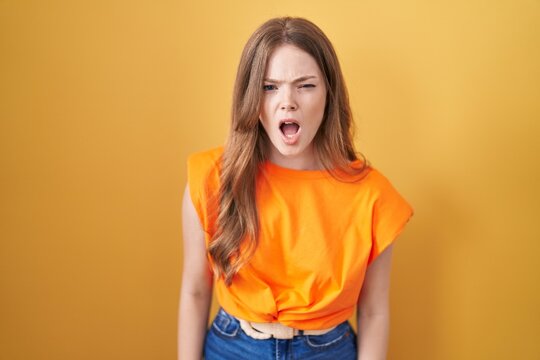 Caucasian woman standing over yellow background angry and mad screaming frustrated and furious, shouting with anger. rage and aggressive concept.