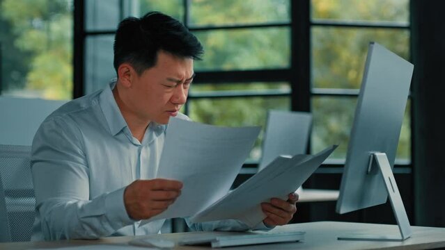 Nervous Asian depressed man lawyer businessman upset senior specialist read financial documents statistical business report work with documentation find mistake difficult task incorrect data in papers
