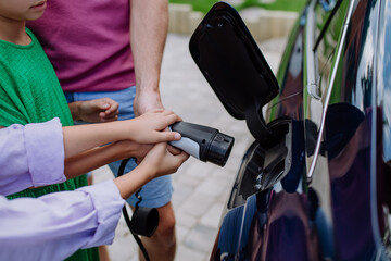 Close-up of father holding power supply cable with his little daughters and charging their electric car.
