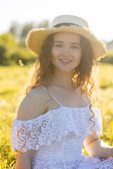 Beautiful smiling young girl in a white dress with curly hair, straw hat, with picnic and bouquet of purple wild flowers