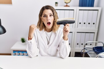 Young hispanic woman working at dentist clinic holding whitening test scared and amazed with open mouth for surprise, disbelief face