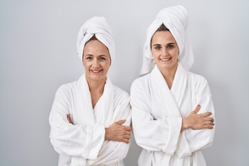 Middle age woman and daughter wearing white bathrobe and towel happy face smiling with crossed arms looking at the camera. positive person.