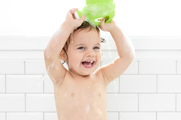 Laughing child rinsing hair in bathtub with watering can