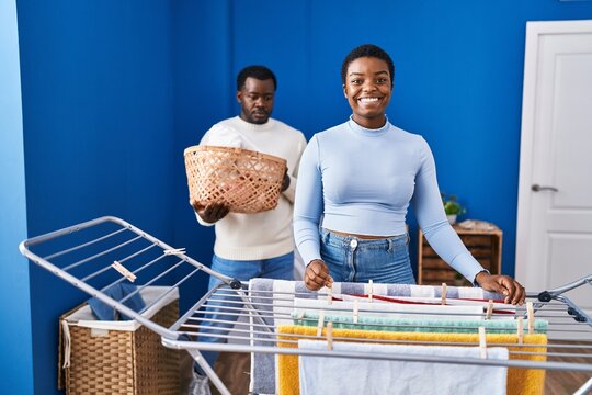 Young african american couple hanging clothes at clothesline looking positive and happy standing and smiling with a confident smile showing teeth