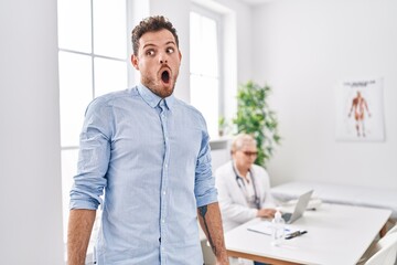 Fototapeta premium Hispanic man at doctor clinic scared and amazed with open mouth for surprise, disbelief face