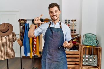 Handsome young man working as manager at retail boutique smiling and confident gesturing with hand doing small size sign with fingers looking and the camera. measure concept.