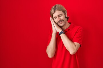 Caucasian man with mustache standing over red background sleeping tired dreaming and posing with hands together while smiling with closed eyes.